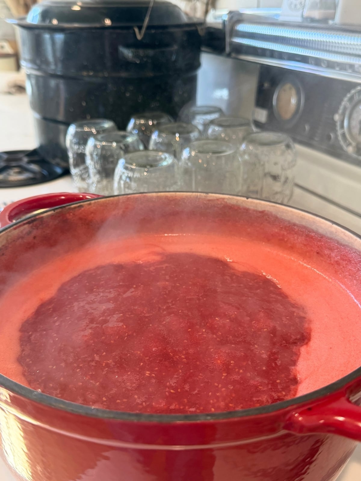 boiling pot of raspberry jam with sterylized pint sized mason jars on the side and the waterbath canner all on the stove top