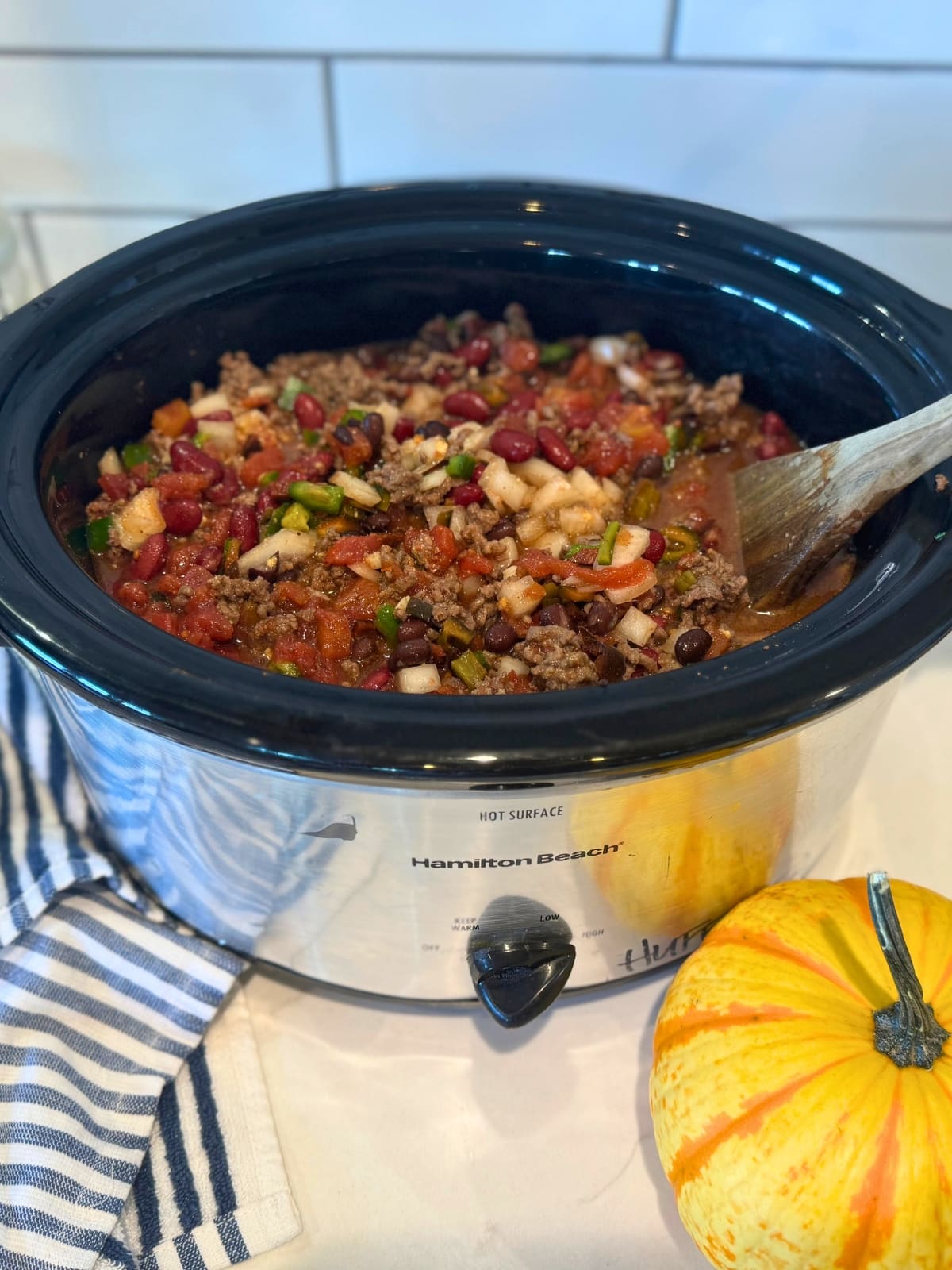 crockpot full of the best chili: beans, peppers, tomatoes, onion, ground beef and a small pimpkin on the side