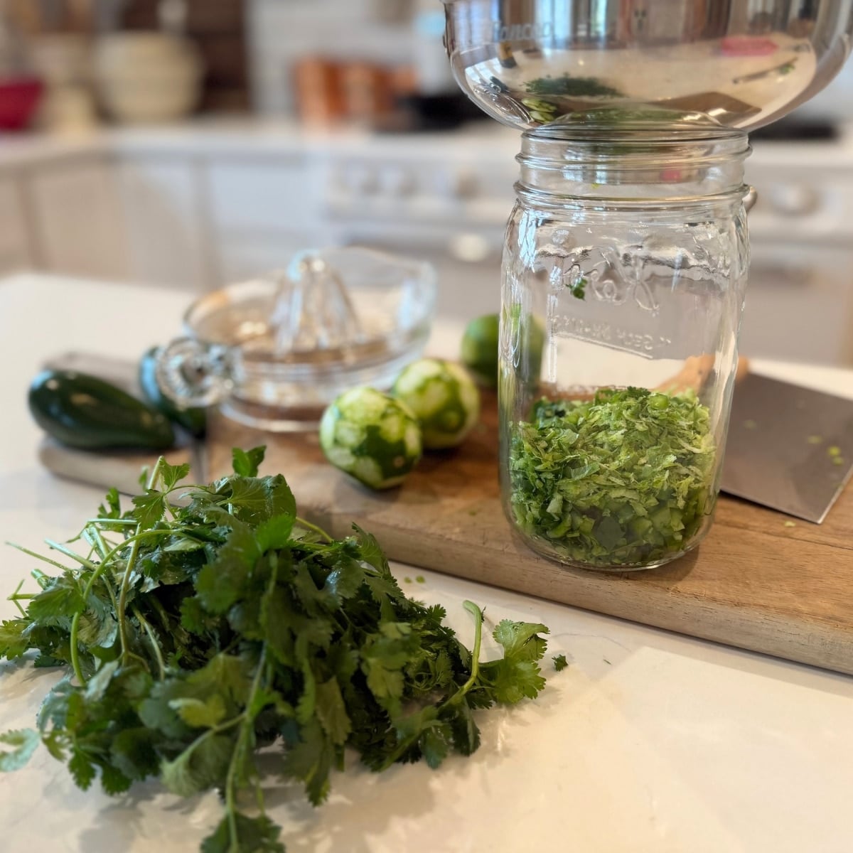ingredinets and tools: wood cutting board with a bench scraper, filet knife, zested limes, and the planer to zest them, a jalapeno and chopped cilantro with a glass juicer