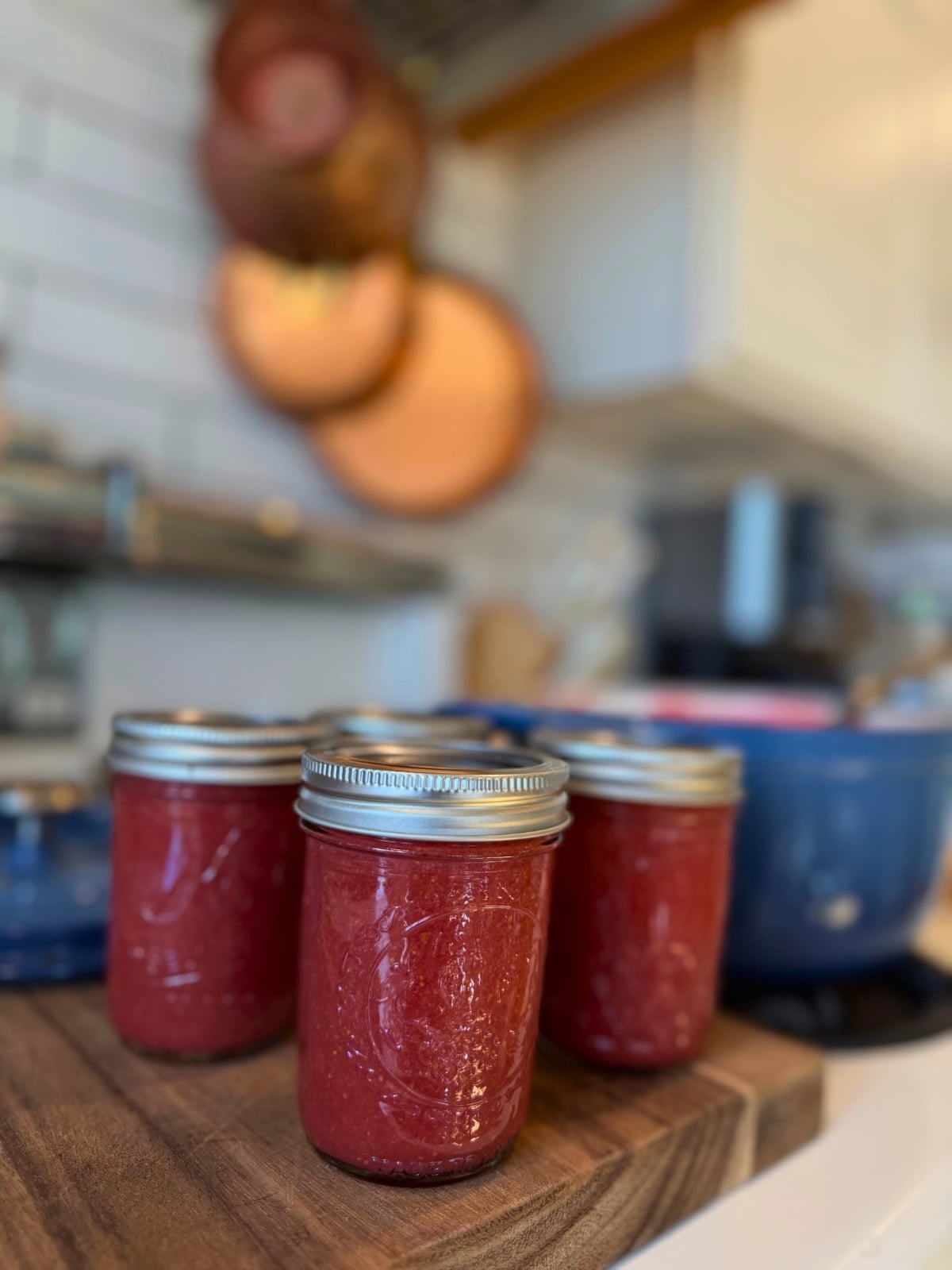 jars of strawberry jam on wood cutting board on stove next to jam pot