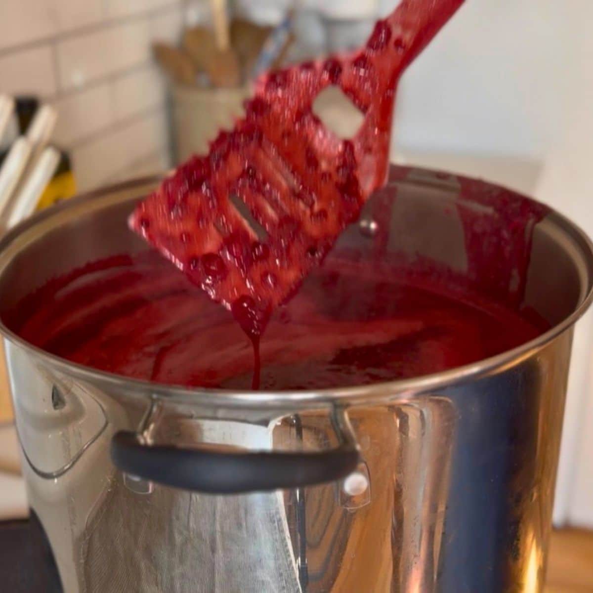 large spatula comming out of a pot of blackberry jam cooking on stove top