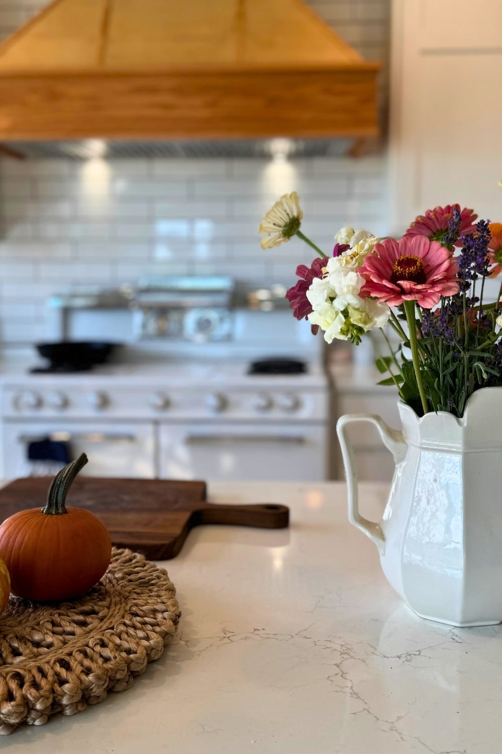 my farmhouse kitchen with stove and hood ven tin background and piumpkin, cutting board and vase of flowers on counter