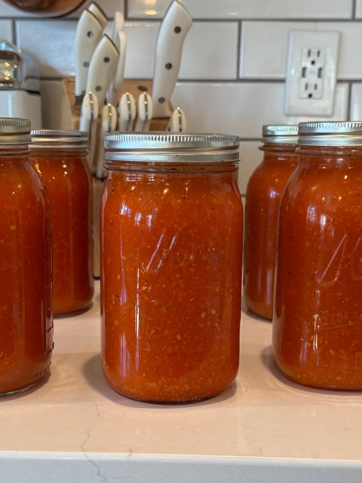 quart sized mason jars full of home canned tomato soup on counter with a block of kitchen knives behind them