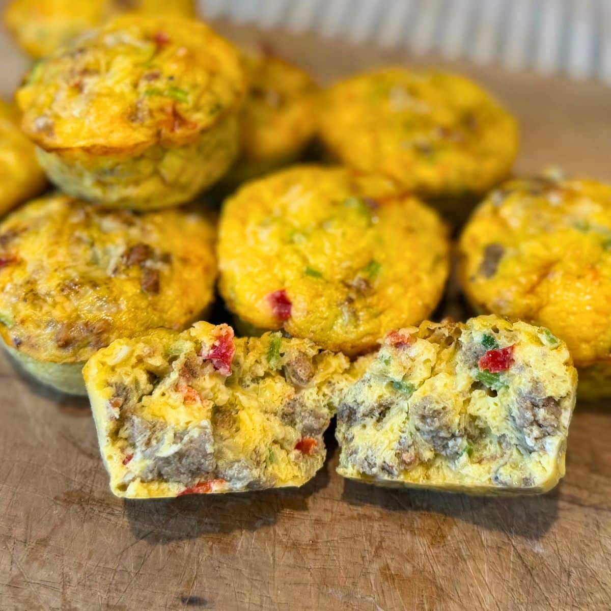 breakfast egg muffins on wood cutting baord with one opened up to show sausage, bacon, peppers, onion and cilantro pieces