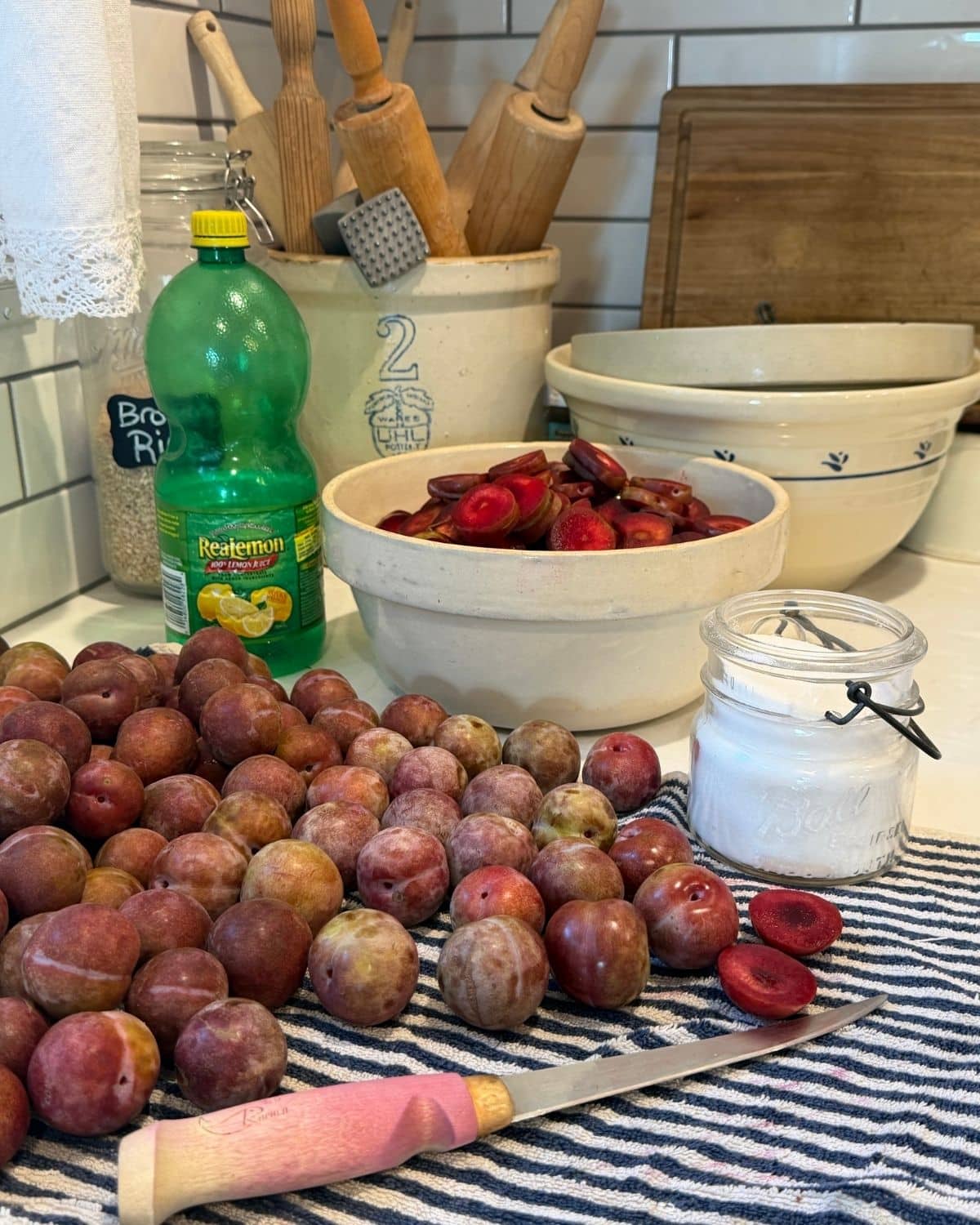 canned plum sauce recipe ingredients on a wash cloth: plums, bottled lemon juice and sugar on counter