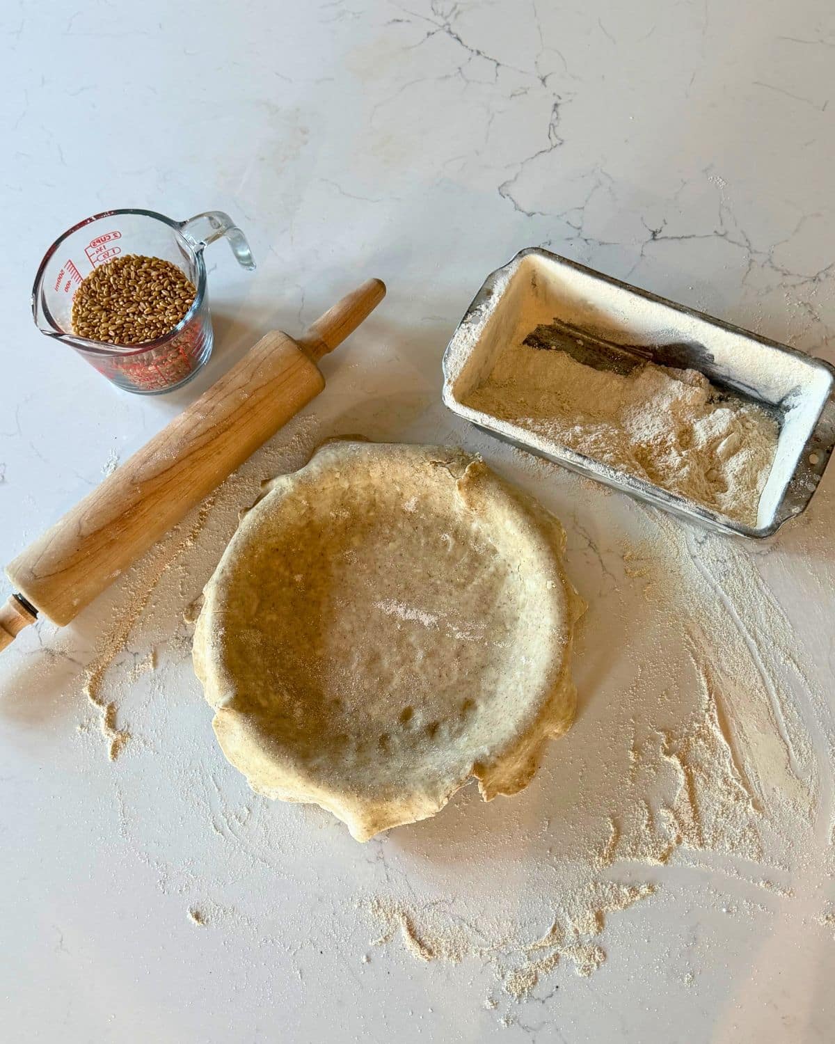 wheat berries, flour, a rolloing pin, and a homemade pie crust in pie pan to demonstrate depression era kitchen habits for cooking from scratch.