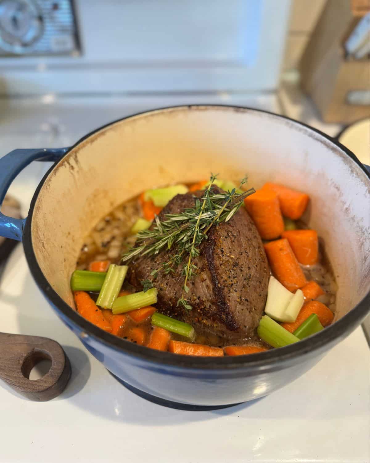 A small rump roast seared in a Dutch oven surrounded by root vegetables, herbs, and rich pan juices to showcase depression era kitchen habits for slow cooking cheap cuts of meat.