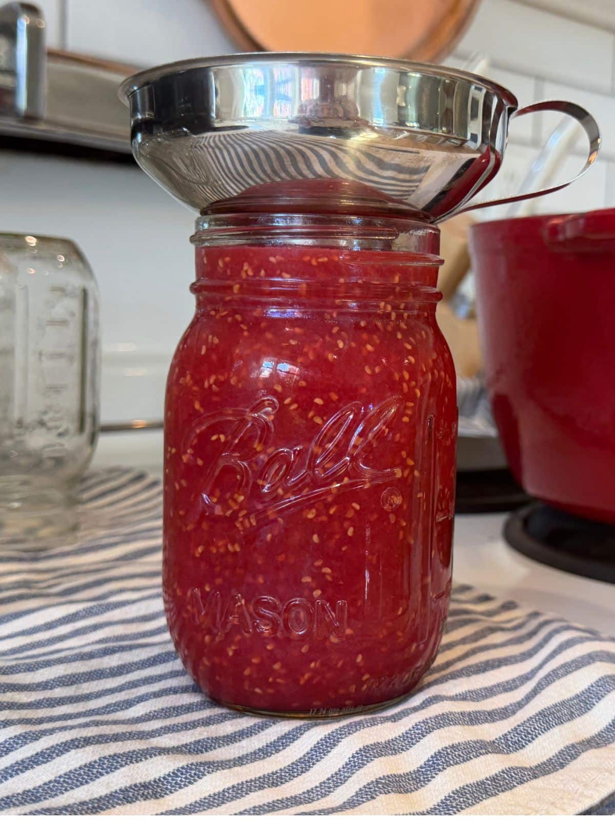filling jar on stove top with hot jam using a funnel
