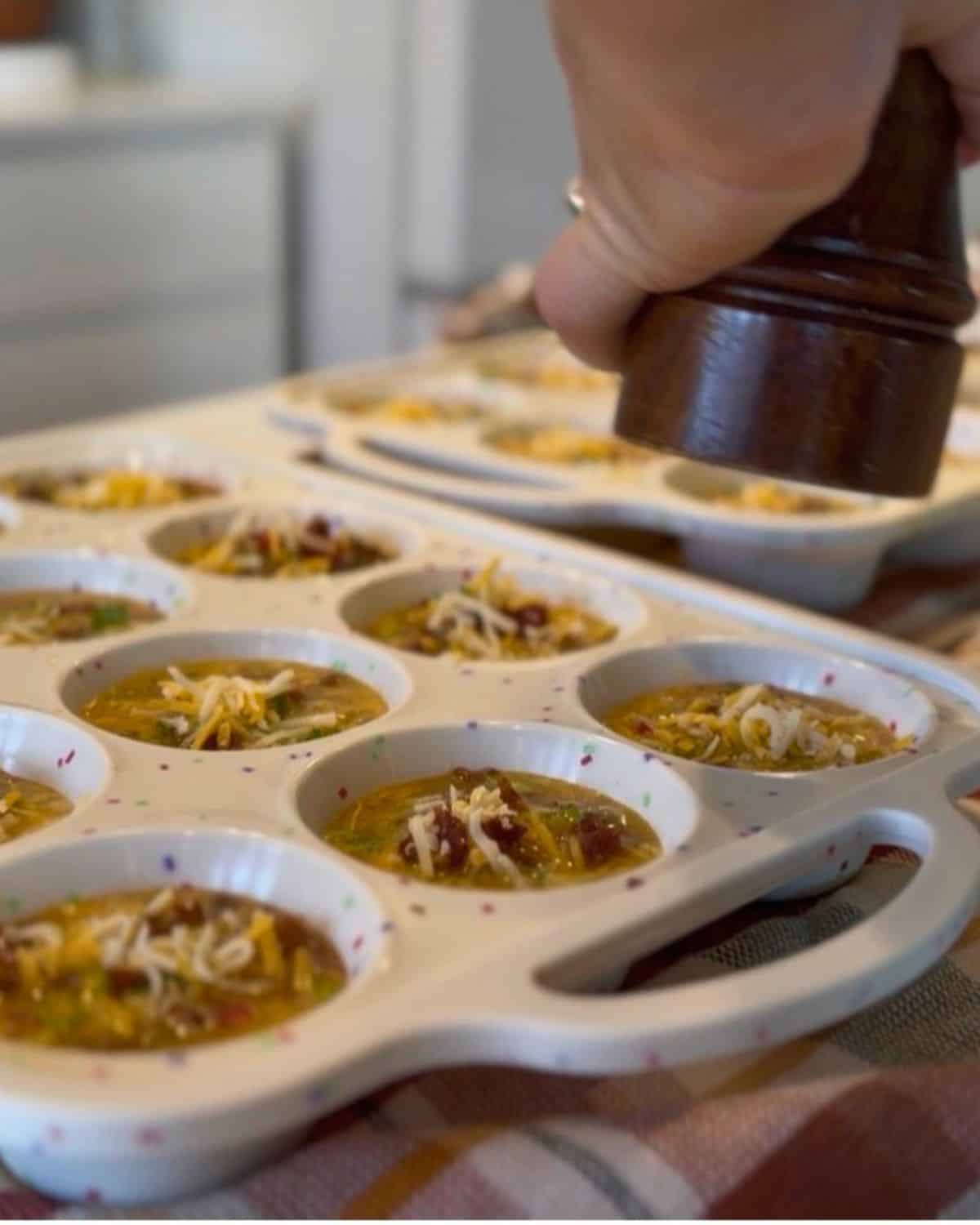 grinding pepper onto tops of uncooked breakfast egg muffins in silicone muffin baking dishes