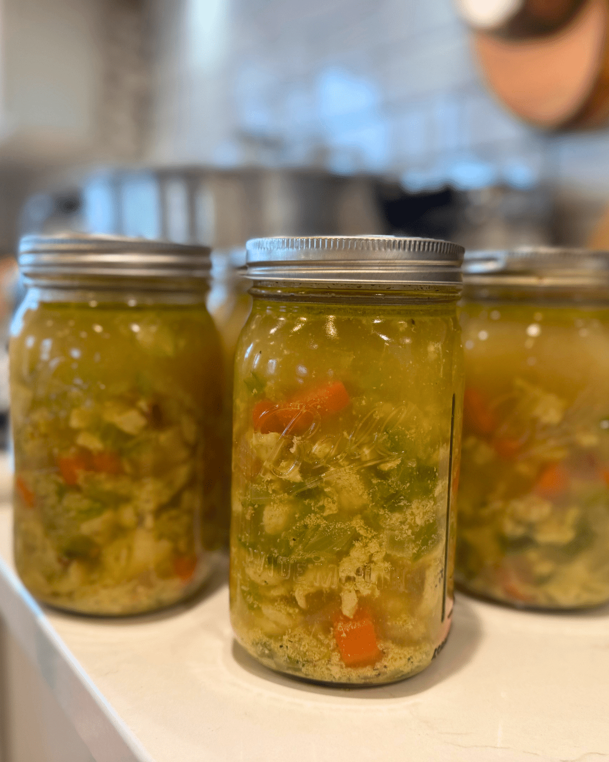 jars of chicken vegetable soup canning recipein quart jars on the counter with the pressure canner in the background
