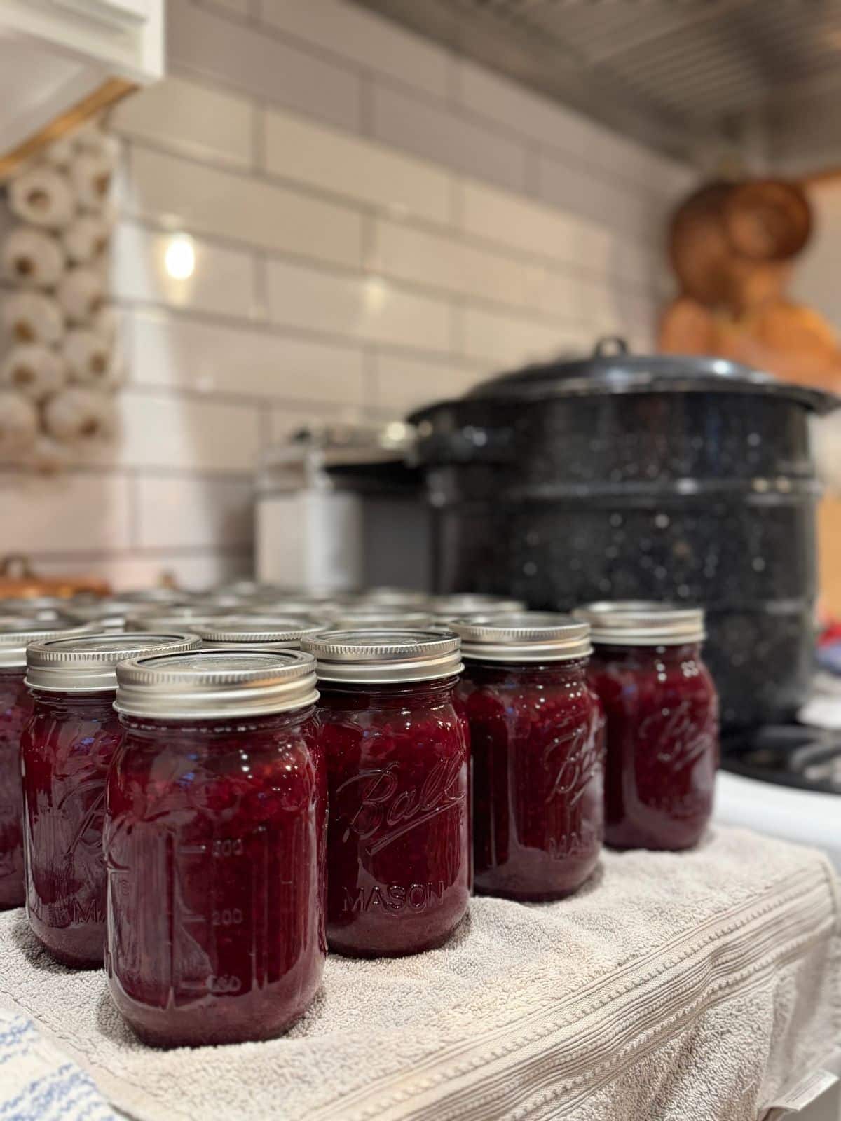 jars of jam cooling on counter next to a wat bath canner on the stove top