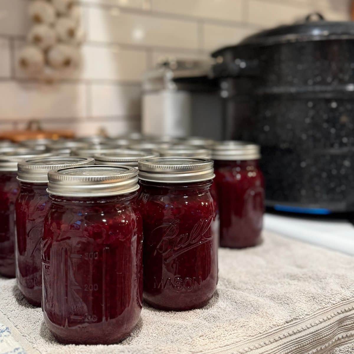 jars of jam cooling on counter with water bath canner on stove top