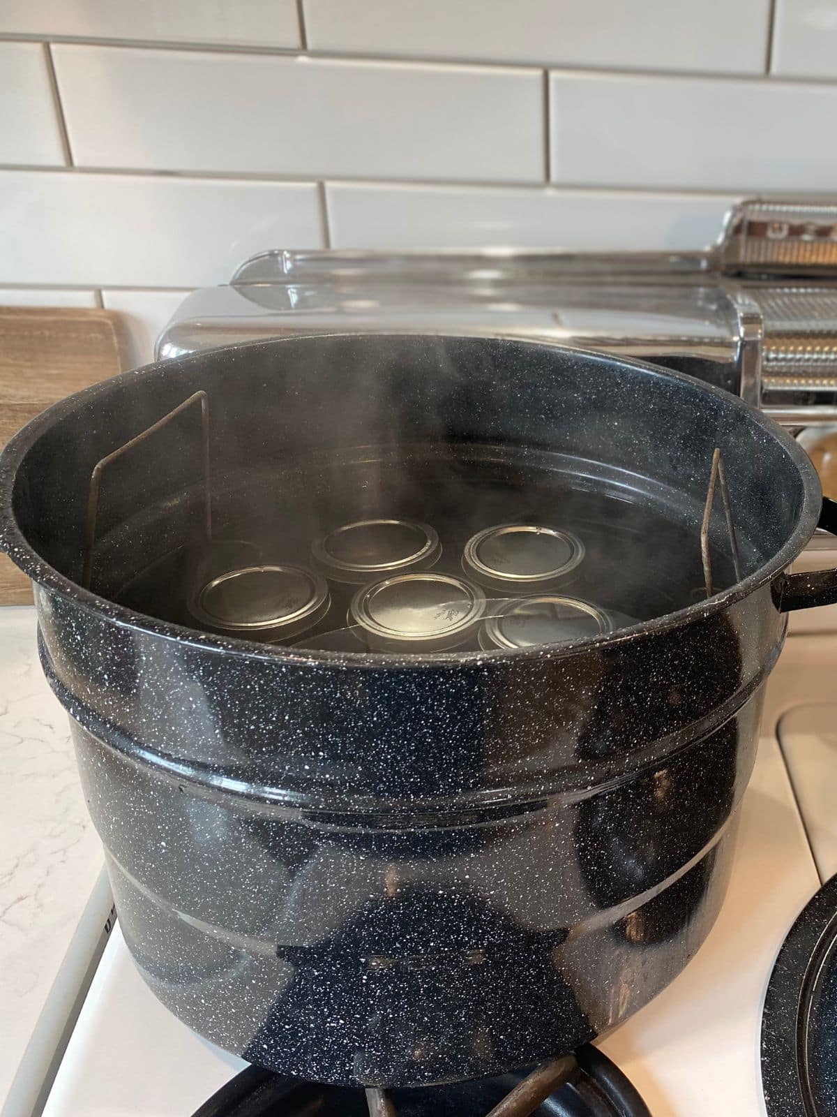 water bath canner on stove top filled with hot water, jars and jar rack