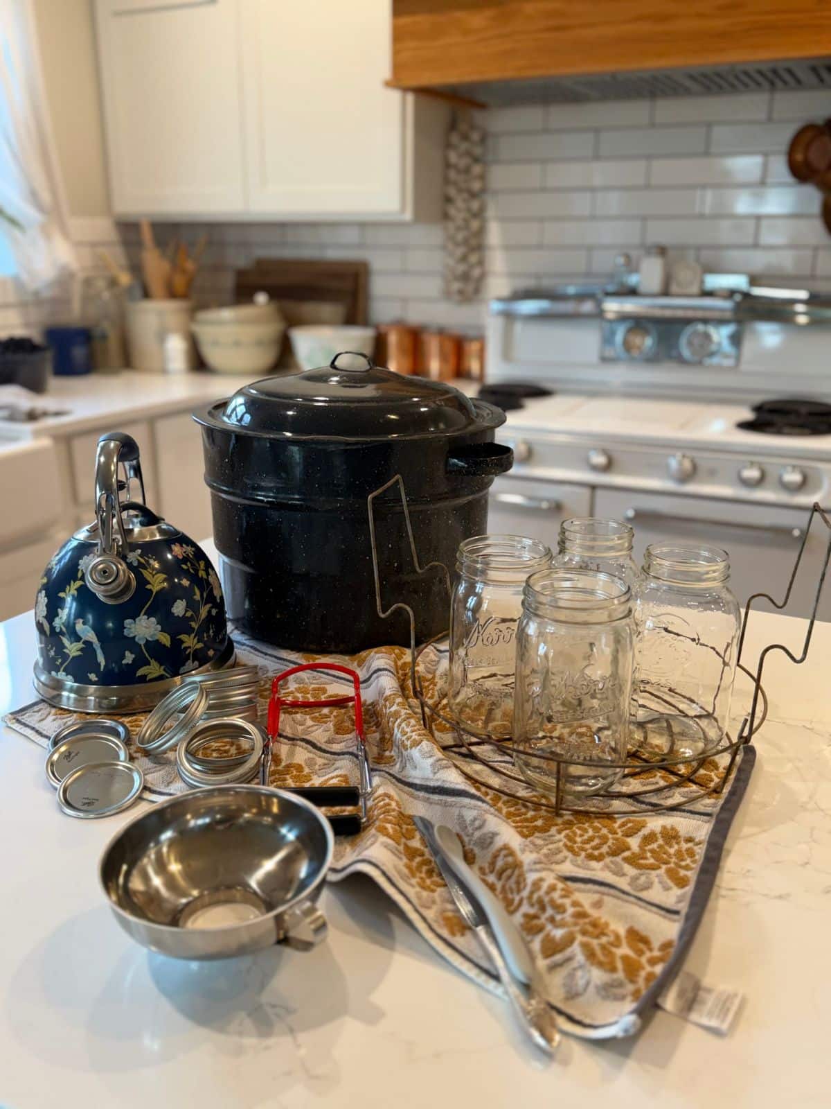 water bath canning equiptment: water bath canner, water kettle, lids, bands, jars, a jar rack or canner rack, jar lifter, funnel, debubbling tools all on the counter