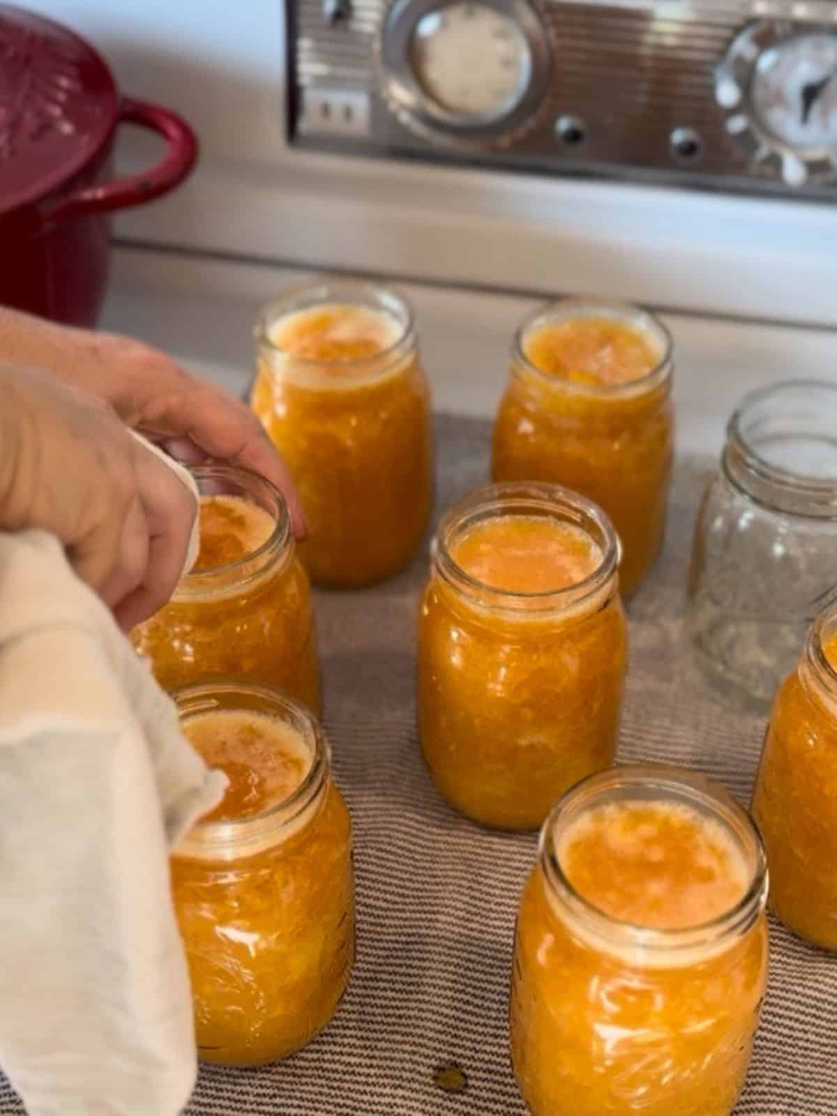 wiping rims of canning jars filled with peach jam