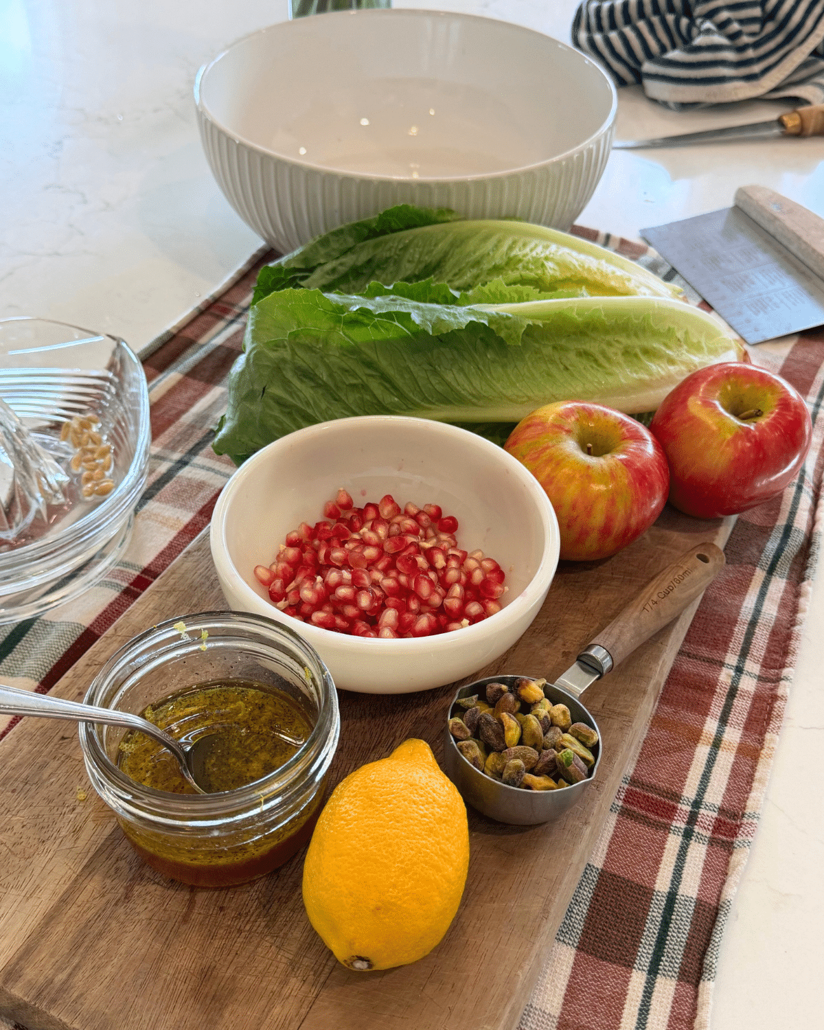 a large salad bowl, romain lettuce, pomagranite seeds, apples and pistachios with the homemade dressing and a lemon on a wood cutting board for autumn salad