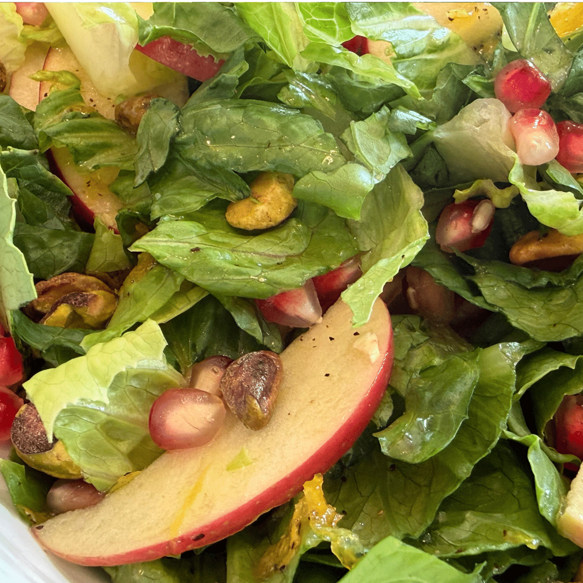 autumn salad -autumn apple salad - fresh romain lettue tollsed with thin sliced red apples, pomegranites seeds and pistachos with a lemon vinegrette