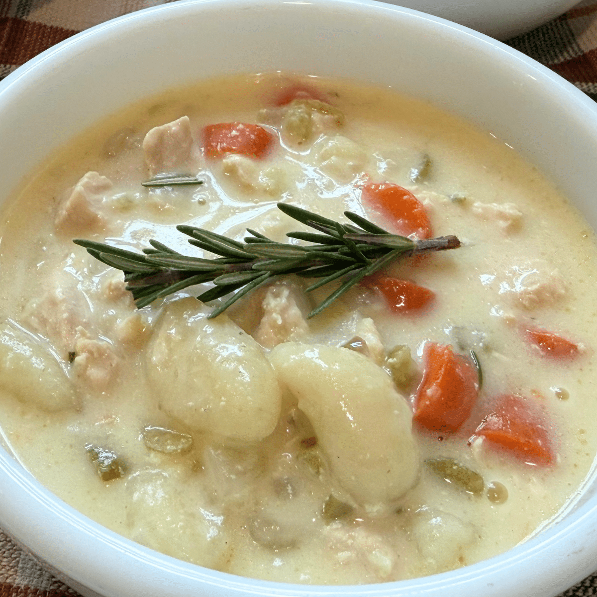 creamy chicken gnocci soup in a white bowl garnished with a sprig of rosemary